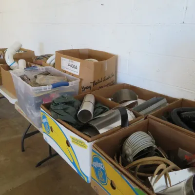 Sale Photo Thumbnail #61: Assorted hardware, plumbing, and building supplies arranged in cardboard boxes and plastic totes on a folding table.