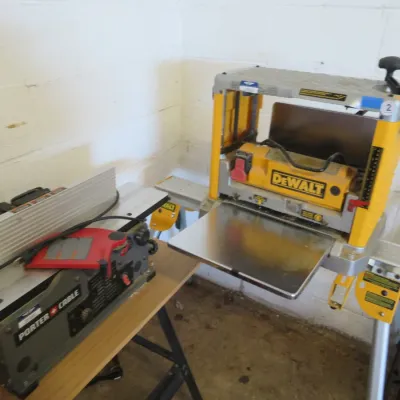 Sale Photo Thumbnail #19: DeWalt portable thickness planer mounted on a stand, displayed alongside a Porter-Cable benchtop jointer.