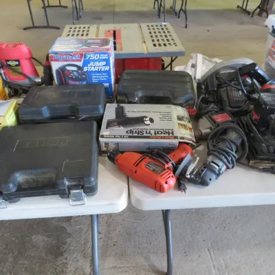 Sale Photo Thumbnail #44: Assortment of power tools and equipment, including drills, sanders, a heat gun, and a Duralast jump starter on folding tables.