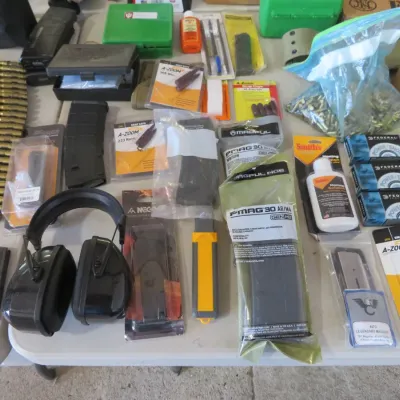 Sale Photo Thumbnail #56: Large assortment of shooting supplies, including belted ammunition, boxed 223 Remington ammo, Magpul PMAG 30 magazines, snap caps, and hearing protection headphones.