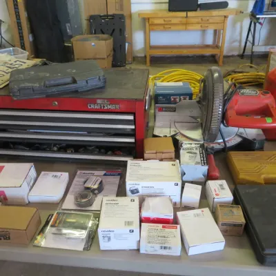 Sale Photo Thumbnail #28: A table filled with workshop tools and hardware including a red Craftsman metal tool chest, a miter saw, compressed gas cylinder, and various boxed electronics and replacement parts.