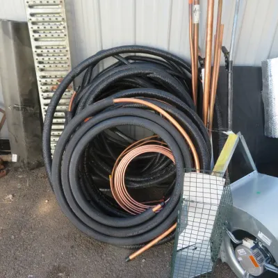 Sale Photo Thumbnail #48: Assorted HVAC and construction supplies including coils of insulated black line set tubing, copper pipe, and a metal blower fan housing.