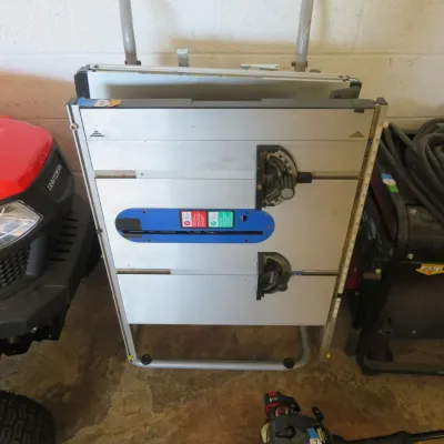 Sale Photo Thumbnail #10: Portable jobsite table saw with a folding stand and integrated handles, shown stored vertically next to power equipment.