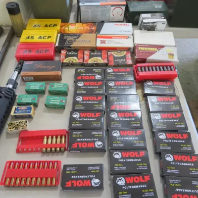 Sale Photo Thumbnail #57: Large assortment of ammunition, reloading trays, and firearm barrels arranged on a table, including Wolf Polyformance .223 Rem and various handgun calibers.