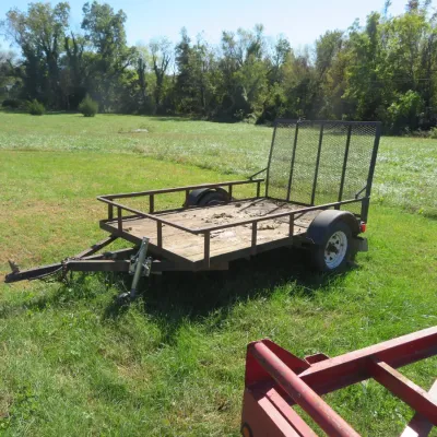 Sale Photo Thumbnail #65: Single-axle utility trailer featuring a wooden deck, metal side rails, and an upright mesh rear ramp gate.