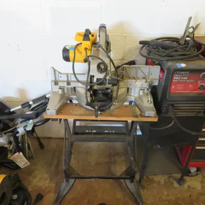 Sale Photo Thumbnail #14: DeWalt compound miter saw mounted on a metal folding stand, positioned alongside a Maxus Pro-140 MIG/Flux welder.