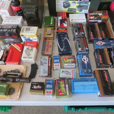 Sale Photo Thumbnail #51: Large collection of assorted ammunition boxes, rifle scope, and shooting accessories displayed on a table.
