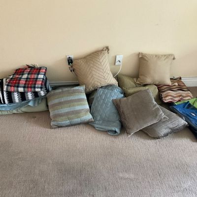 Sale Photo Thumbnail #139: Collection of assorted throw pillows, folded blankets, and textiles lined up along a wall.