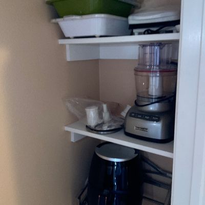 Sale Photo Thumbnail #132: Pantry shelves stored with kitchen appliances including a KitchenAid food processor, a black air fryer, and assorted baking dishes.