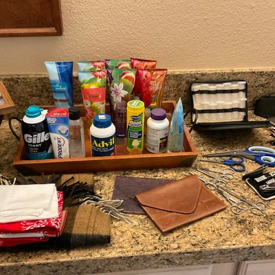 Sale Photo Thumbnail #159: Assortment of personal care items, toiletries, lotions, grooming tools, and accessories displayed on a granite countertop with a wooden tray.