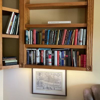 Sale Photo Thumbnail #54: Built-in oak shelving units filled with various hardback and paperback books, situated above framed artwork on a neutral wall.