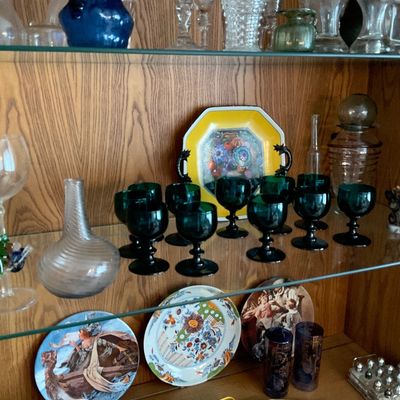 Sale Photo Thumbnail #129: Wooden display cabinet filled with collectible glassware, decorative plates, and dark green goblet set.