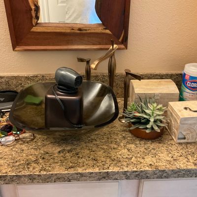 Sale Photo Thumbnail #158: Bathroom vanity counter display featuring a dark glass vessel sink, various sunglasses and eyeglasses, decorative carved wooden boxes, and a small artificial succulent plant.