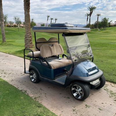 Sale Photo Thumbnail #2: Metallic blue four-seater golf cart with tan upholstered seating, custom chrome wheels, foldable windshield, and a roof canopy.