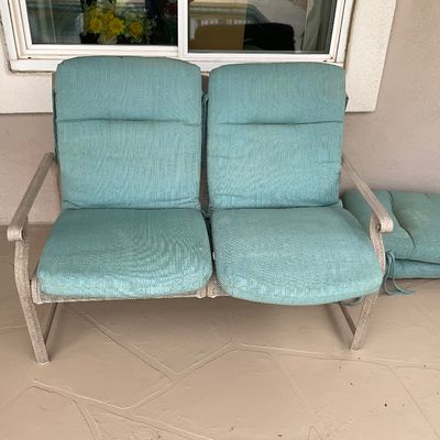 Sale Photo Thumbnail #41: Outdoor patio bench with a metal frame and teal upholstered cushions, accompanied by additional matching cushions stacked nearby.