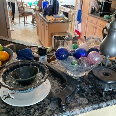 Sale Photo Thumbnail #100: Kitchen island filled with home goods including decorative glass orb spheres in a crystal bowl, a metal samovar urn, studio pottery bowls, and wooden stands.