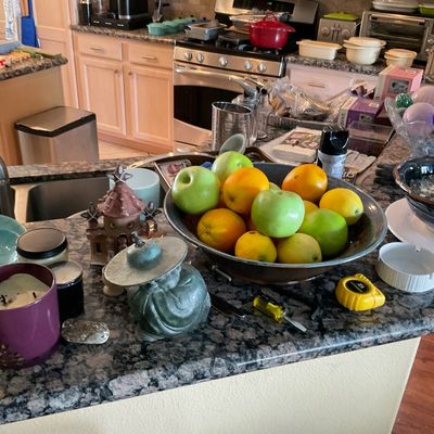 Sale Photo Thumbnail #99: Assorted kitchenware and home decor items displayed on a granite countertop, including artificial fruit in a bowl, decorative figurines, and candles.