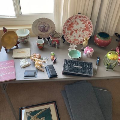 Sale Photo Thumbnail #147: Collection of tabletop decor and collectibles including transferware plates, small ceramic figurines, a frog-shaped lantern, a book, and small leather goods.