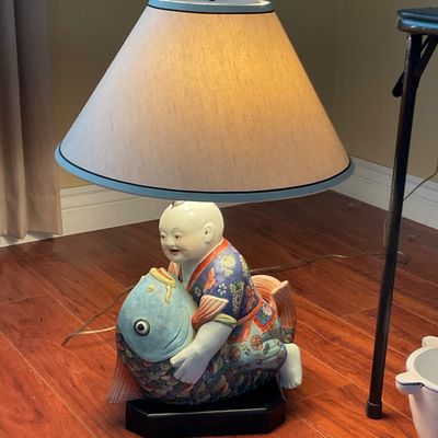 Sale Photo Thumbnail #79: Vintage Asian porcelain table lamp featuring a figurine of a child riding a large blue koi fish, mounted on a black base with a cone-shaped shade.