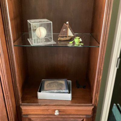 Sale Photo Thumbnail #68: Tall wooden display cabinet featuring glass shelves and lower drawers, holding various decorative items including a boxed baseball and a miniature sailboat.