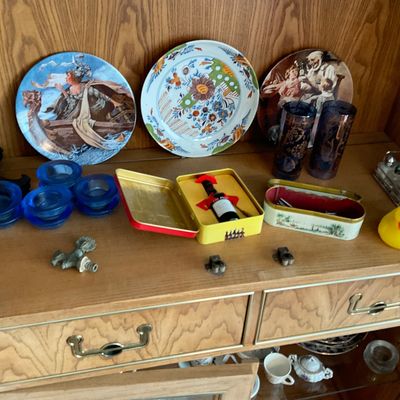 Sale Photo Thumbnail #128: Collection of decorative collectibles displayed in a wooden cabinet, including illustrative plates, cobalt blue glassware, small tins, and novelties.
