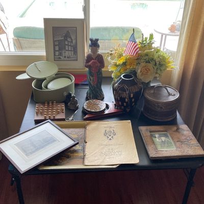 Sale Photo Thumbnail #57: Tabletop display featuring framed artwork, decorative ceramic and wooden boxes, an Asian figurine, a patterned vase, floral arrangement, and vintage printed ephemera.