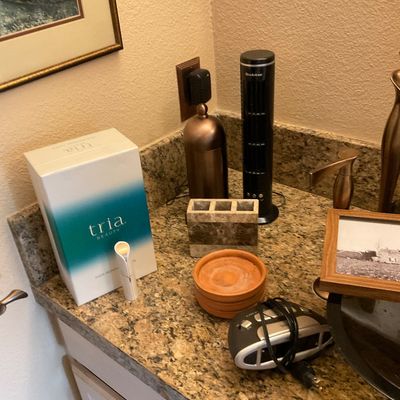 Sale Photo Thumbnail #164: Tria Beauty hair removal laser system with box, shown alongside various bathroom counter accessories, a Brookstone tower device, and a small digital alarm clock.