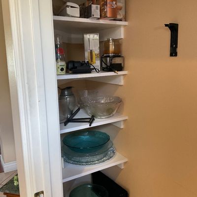 Sale Photo Thumbnail #133: Pantry closet filled with various kitchenware including a food processor, boxed appliances, serving pitchers, and teal glass mixing bowls.