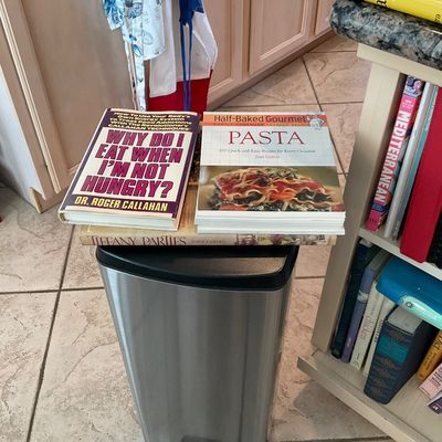 Sale Photo Thumbnail #110: A stainless steel step trash can displaying cookbooks on top, including 'Why Do I Eat When I'm Not Hungry?' and 'Half-Baked Gourmet Pasta'.