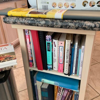 Sale Photo Thumbnail #111: Small wooden kitchen cart with a granite top and built-in shelves filled with assorted cookbooks and binders.