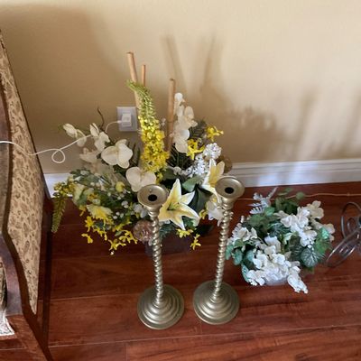 Sale Photo Thumbnail #84: Pair of tall brass spiral candlestick holders resting on the floor alongside decorative faux floral arrangements.