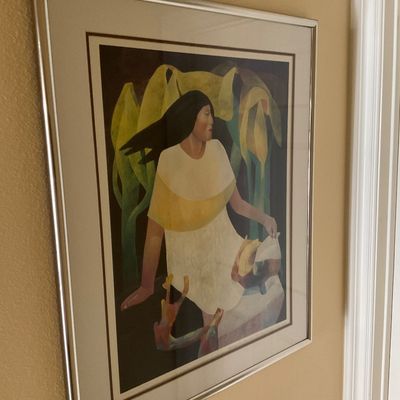 Sale Photo Thumbnail #138: Framed Southwest-style art print depicting a woman among calla lilies, presented in a silver-toned metal frame with double matting.