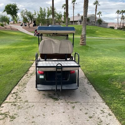 Sale Photo Thumbnail #7: Golf cart featuring beige vinyl seating, a blue roof canopy, and a metal rear cargo rack, parked on a paved path.