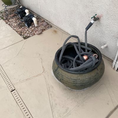Sale Photo Thumbnail #19: Large ceramic garden pot used for hose storage, featuring a coiled grey garden hose attached to an outdoor spigot.