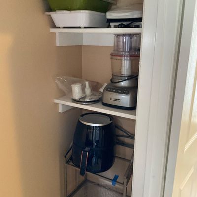 Sale Photo Thumbnail #134: Collection of modern small kitchen appliances, including a KitchenAid food processor, a black air fryer, and plastic serving dishes stored on pantry shelves.