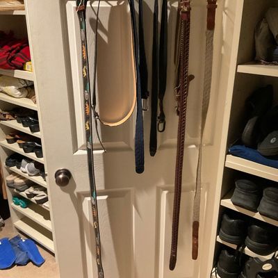 Sale Photo Thumbnail #174: Collection of assorted men's belts hanging from an over-the-door rack inside a closet, including leather, woven, and fabric styles.