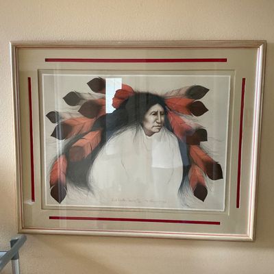 Sale Photo Thumbnail #95: Framed artwork depicting a Native American figure with a feather fan dress, presented under glass with a layered red and cream matting.