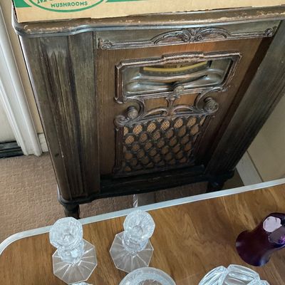 Sale Photo Thumbnail #143: Vintage floor-standing wooden tube radio cabinet with intricate carved trim, alongside assorted clear cut glassware items.