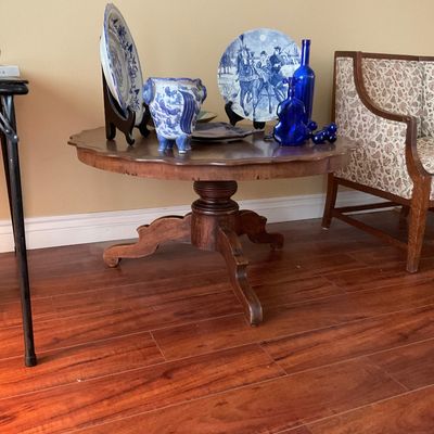 Sale Photo Thumbnail #176: Vintage scalloped-edge wooden pedestal table displaying a collection of blue and white glassware and decorative ceramic plates.