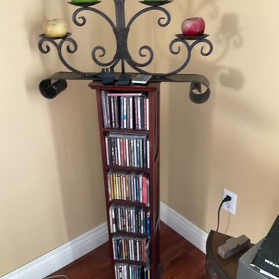 Sale Photo Thumbnail #74: Tall dark wood CD storage tower filled with compact discs, topped with a scrollwork wrought iron candelabra holding apple-shaped candles.