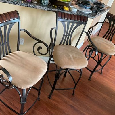 Sale Photo Thumbnail #101: Set of three metal barstools featuring scrollwork armrests, tan upholstered swivel seats, and dark wood crest rails.