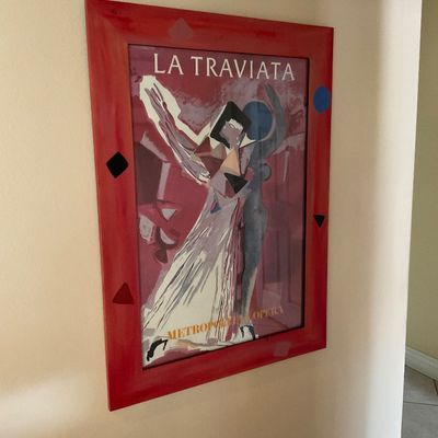 Sale Photo Thumbnail #135: Framed Metropolitan Opera "La Traviata" poster, presented in a red painted wooden frame with hand-painted geometric details.