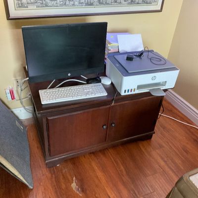 Sale Photo Thumbnail #52: HP all-in-one desktop computer with keyboard and mouse alongside an HP Smart Tank printer, set atop a dark wood two-door cabinet.