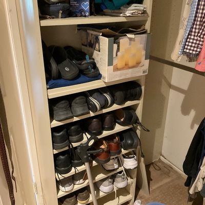 Sale Photo Thumbnail #172: White wooden closet organizer tower filled with assorted men's shoes, boxed pillar candles, medical supplies, and a cane.