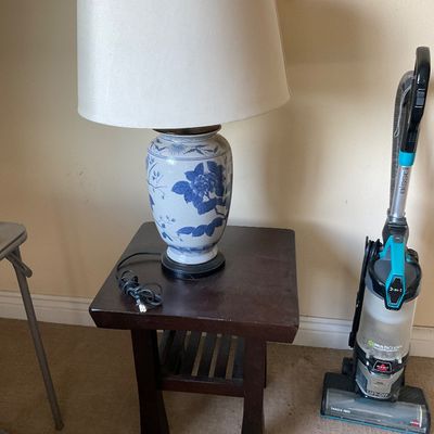 Sale Photo Thumbnail #150: Blue and white porcelain ginger jar table lamp resting on a dark wood end table, alongside a modern Bissell upright vacuum cleaner.
