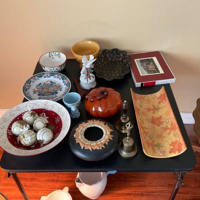 Sale Photo Thumbnail #81: Collection of decorative ceramics, bowls, brass handbells, and seasonal decor, including an orange glazed pumpkin, music note ornaments, and a leaf-patterned tray.