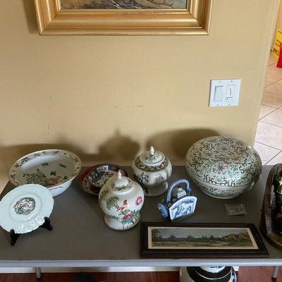 Sale Photo Thumbnail #88: Collection of Asian porcelain ceramics, including ginger jars, decorative bowls, plates, and a small framed landscape print displayed on a folding table.