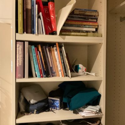Sale Photo Thumbnail #173: Tall white wooden bookcase filled with assorted hardcover and paperback books, medical supplies, small electronics, and household goods.