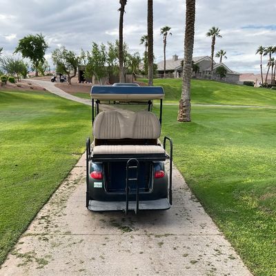Sale Photo Thumbnail #5: Dark blue golf cart featuring tan vinyl seating and a rear step-up platform, parked on a paved golf course path.