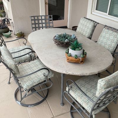 Sale Photo Thumbnail #12: Outdoor patio dining set featuring an oval faux-stone table and six metal chairs with patterned cushions.